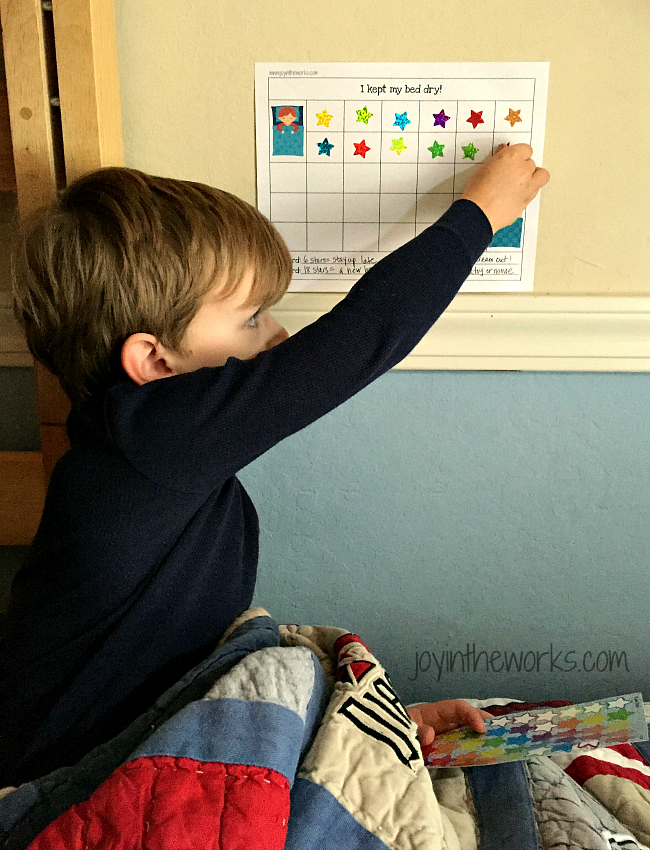 Boy putting star on bedwetting chart for keeping his bed dry