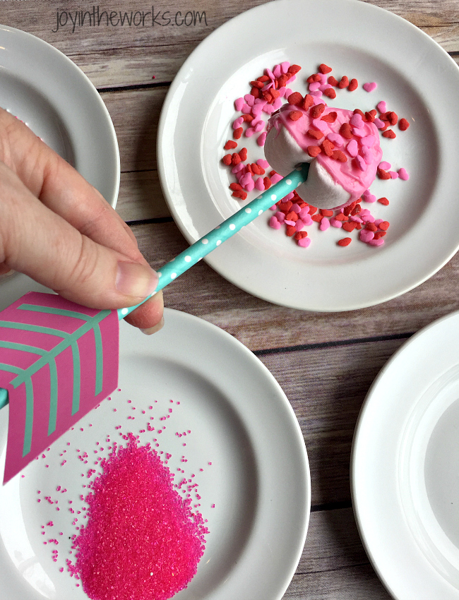 Easy Valentine treat: Cupid's Marshmallow Arrows with dipped and coated heart marshmallows on an arrow straw! No candy dipping necessary however- simply add sprinkles for a festive Valentine sweet! Perfect for a class Valentine party or a Valentine's Day gift!