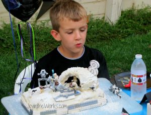 Birthday boy blowing out the candles on his Lego Star Wars Hoth Cake.